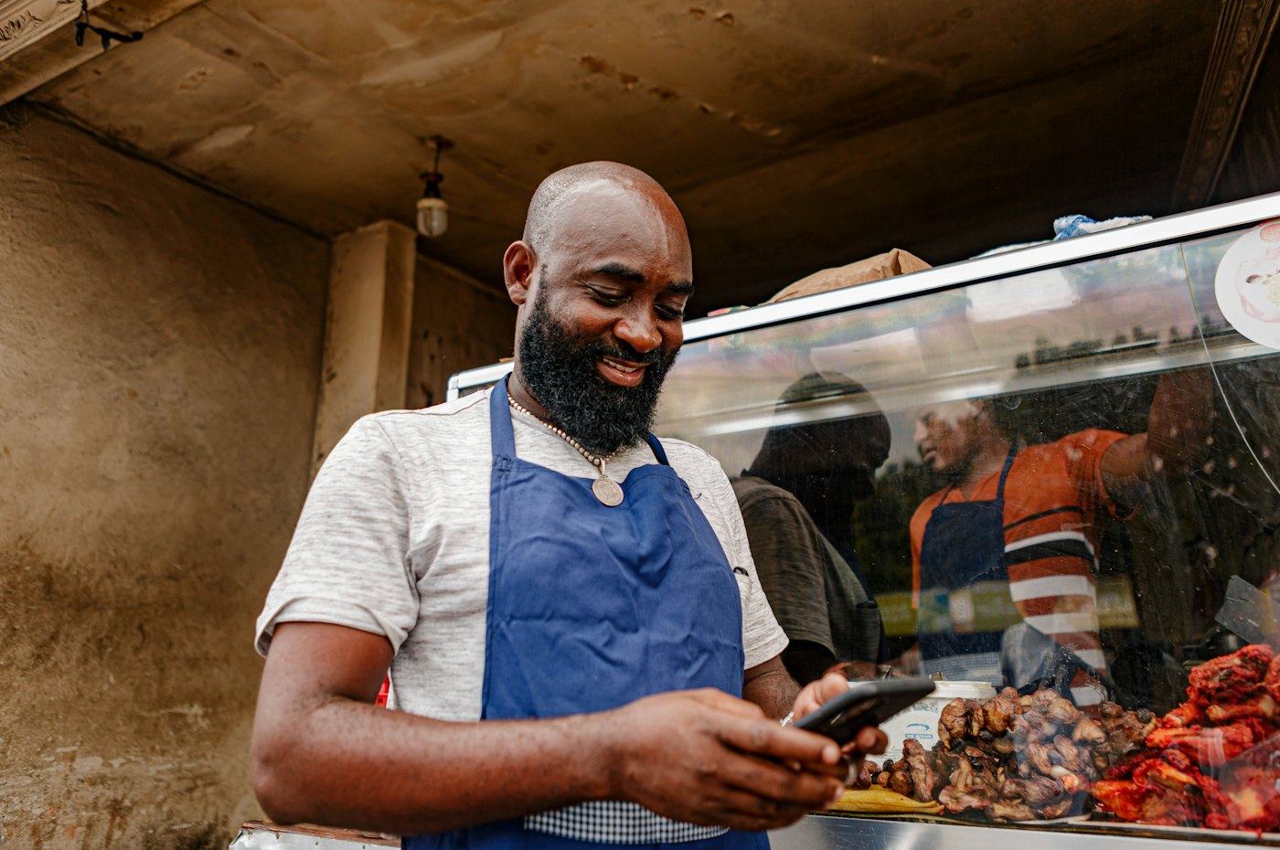 A smiling business owner in an apron checking orders on his phone