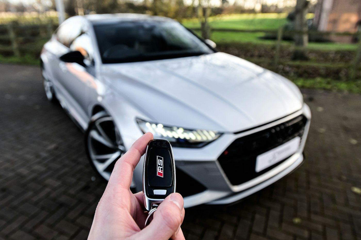A hand holding a car key in front of a new silver car